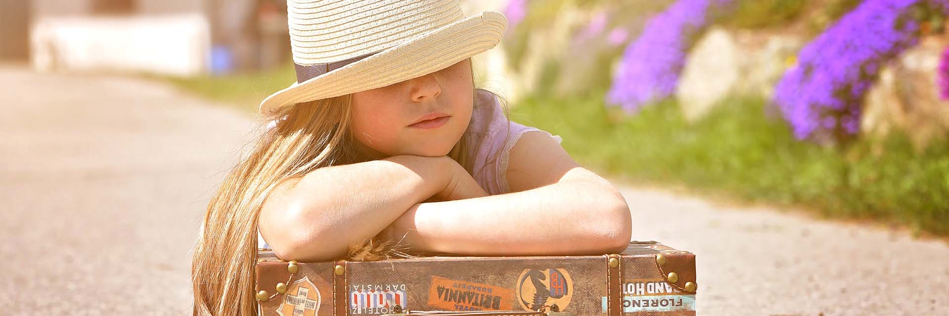 Kind mit Sommerhut stützt sich auf Koffer